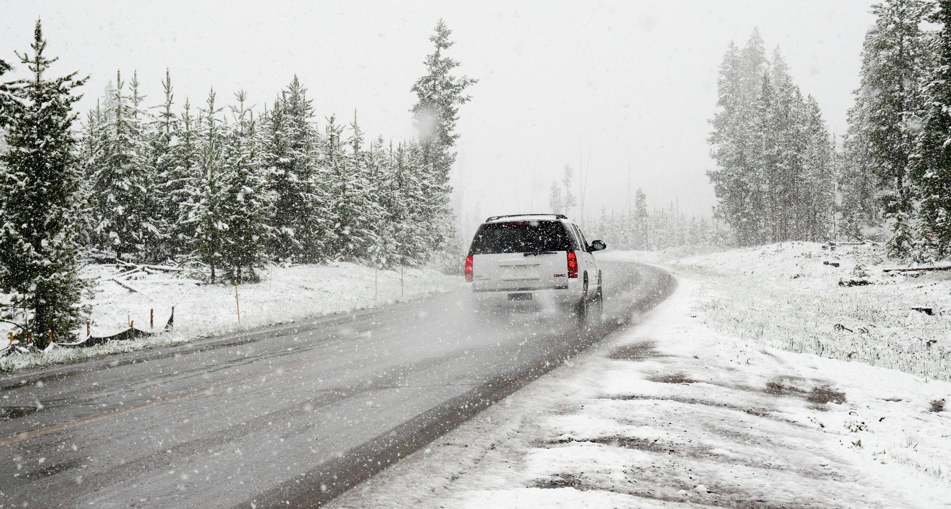 SUV drives on a snowy road through a forest; trees are snow-covered, overcast sky.