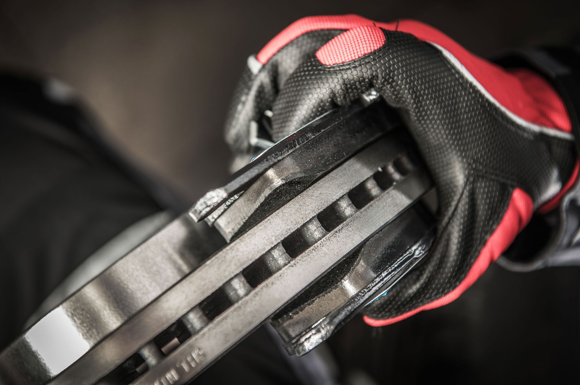 Gloved hand holding two new brake rotors, close-up shot. Red and black glove.