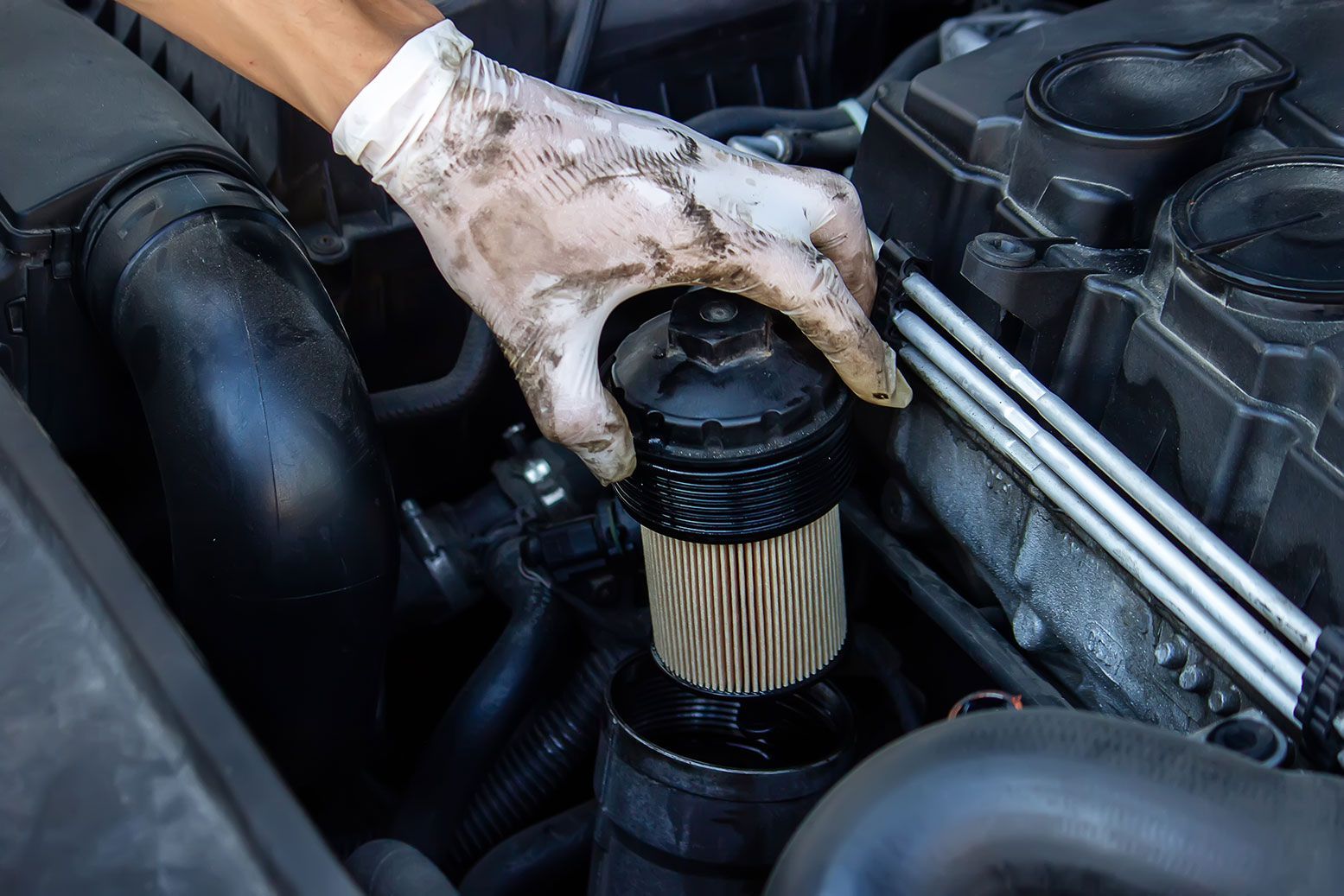 Gloved hand removing an oil filter from a car engine.